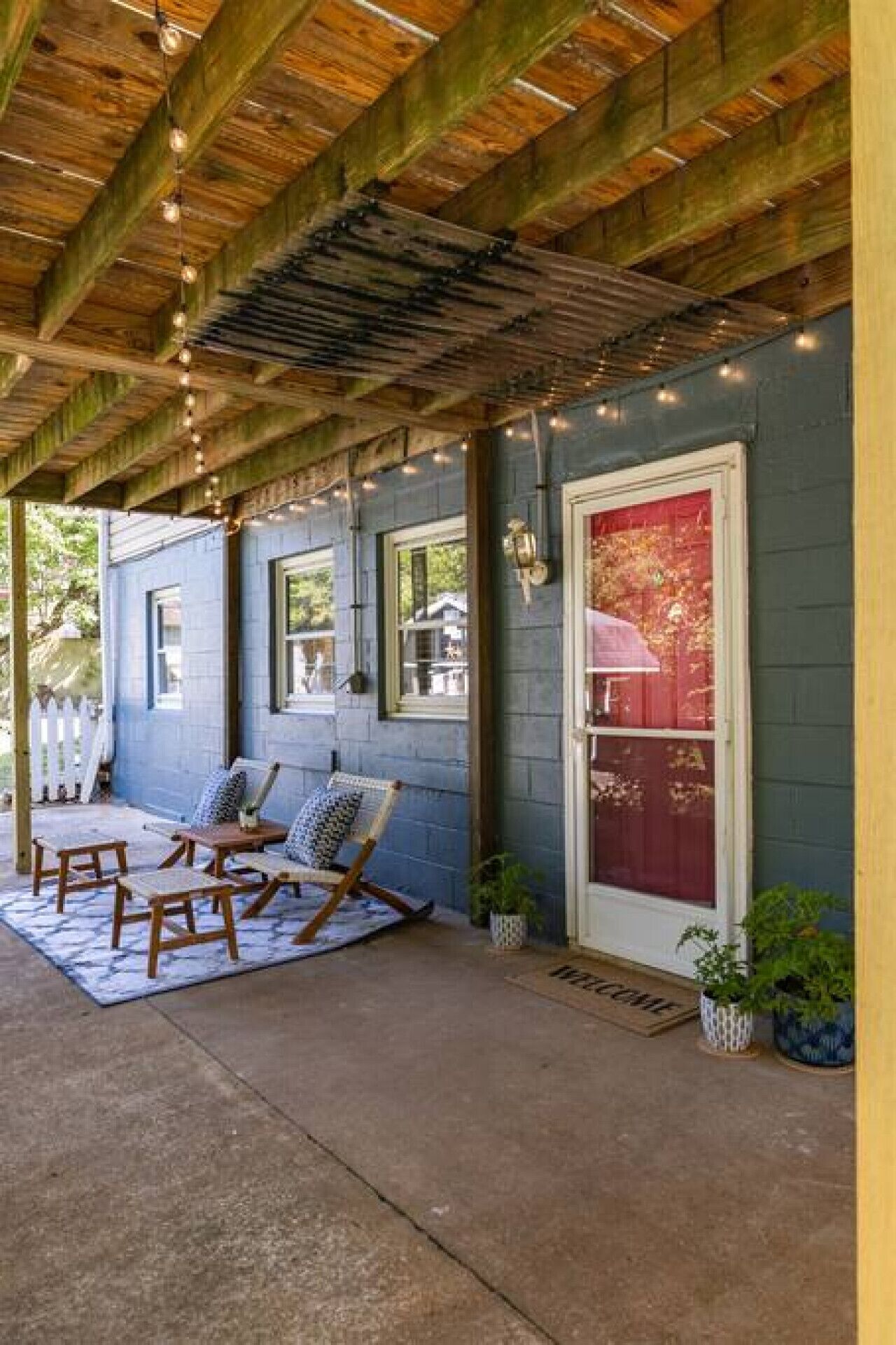 A covered porch with wooden beams, a red door, and a seating area with two chairs and a table.