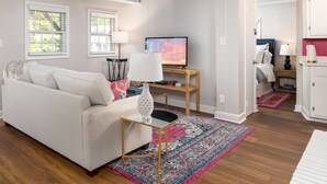 A living room with a white sofa, a TV on a wooden stand, a patterned rug, and a small table with a lamp.