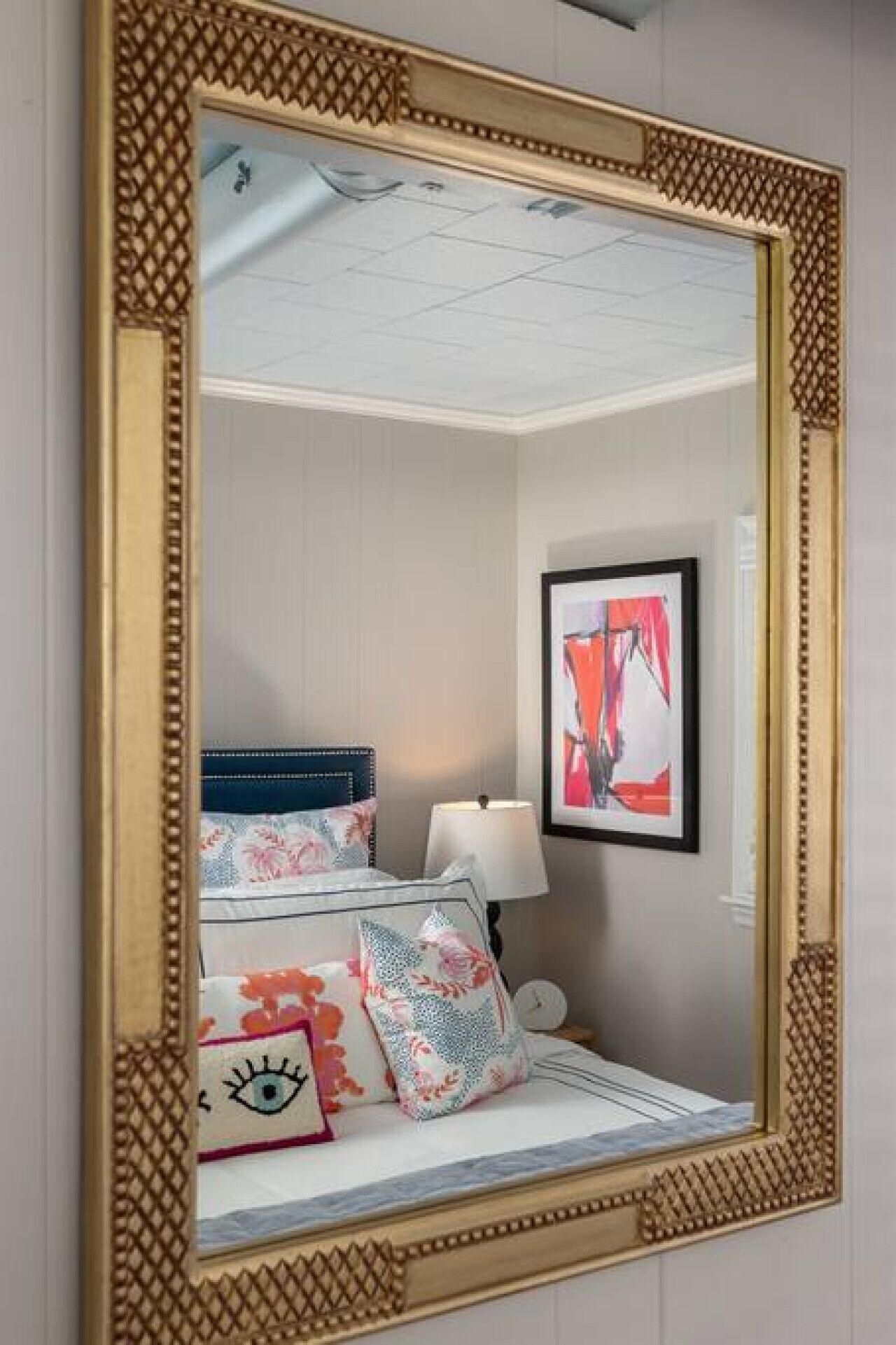A bedroom with a large mirror, a bed with floral bedding, a nightstand, and a framed artwork on the wall.