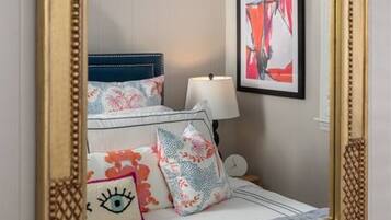 A bedroom with a large mirror, a bed with floral bedding, a nightstand, and a framed artwork on the wall.
