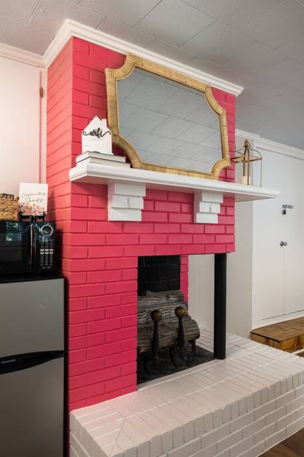 Una chimenea de ladrillo rojo con un fachaleta blanca y un espejo con marco dorado encima.