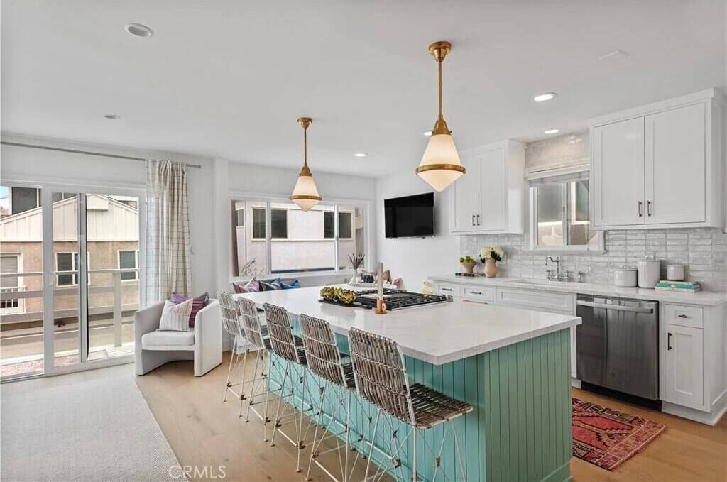 A modern kitchen with white cabinets, a large island with bar stools, pendant lighting, and a sliding glass door to the outside.