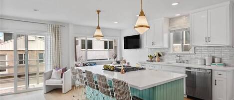 A modern kitchen with white cabinets, a large island with bar stools, pendant lighting, and a sliding glass door to the outside.