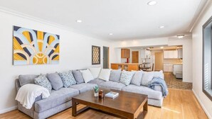 A modern living room with a sectional sofa, a coffee table, and a kitchen in the background. - Spacious 3 BR Modern Home in Grosse Pointe Park (Grosse Pointe Park)
