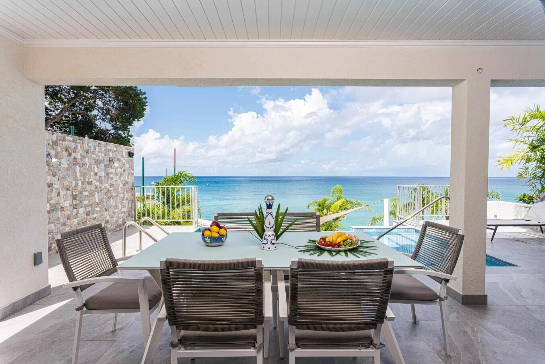 Un coin repas avec vue sur l’océan, comprenant une table avec des chaises, un bol décoratif et une assiette de fruits.