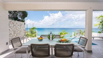 Un coin repas avec vue sur l’océan, comprenant une table avec des chaises, un bol décoratif et une assiette de fruits.