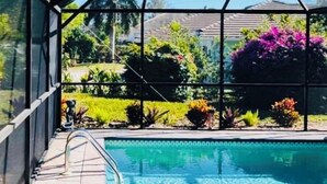 Een overdekt zwembad met uitzicht op een tuin en een huis op de achtergrond.