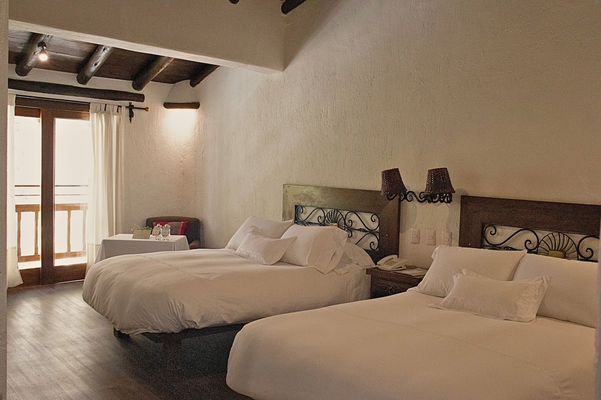 Ein Hotelzimmer mit zwei Betten, einem kleinen Tisch mit Lampe und Blick nach draußen.