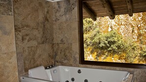 Ein Badezimmer mit einer Badewanne, einem Fenster mit Blick auf Bäume und einer Holzzieldecke.