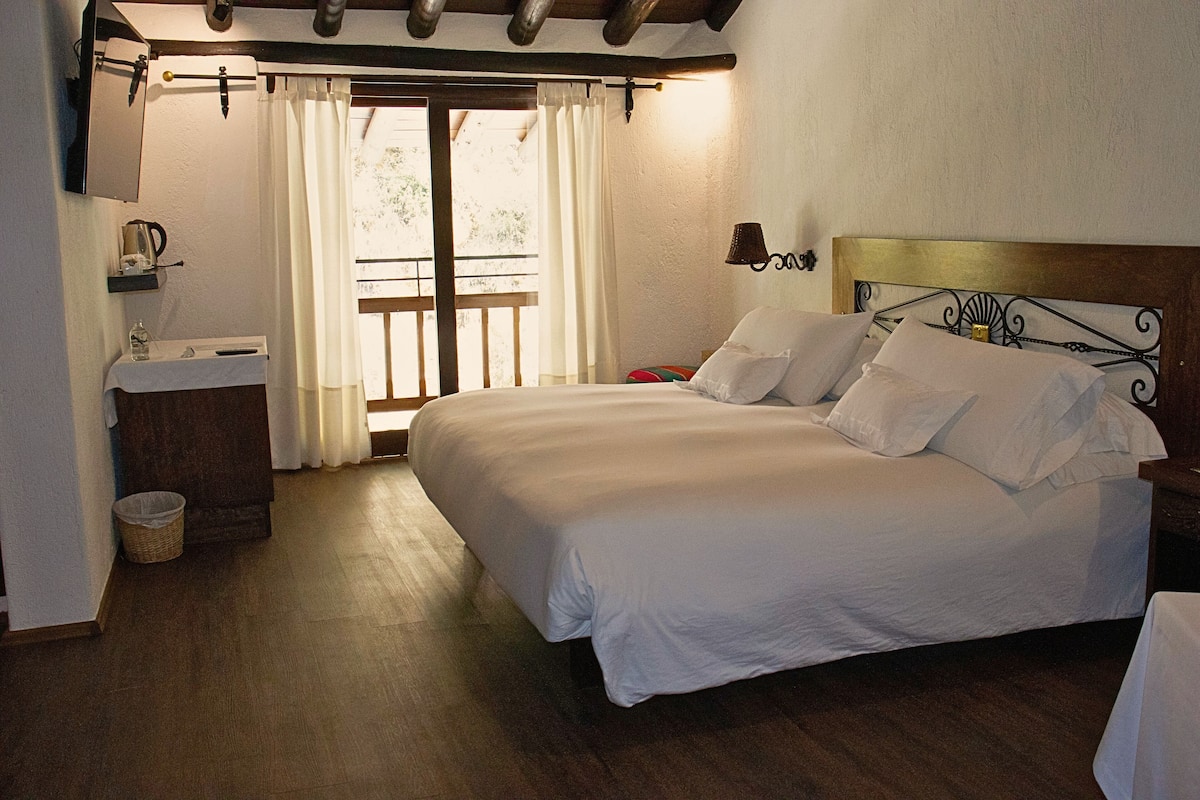Ein Schlafzimmer mit einem großen Bett, einem Holz-Kopfteil, einem Nachttisch, Vorhängen an einem Fenster und einem Balkon.