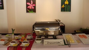 Ein Buffet mit verschiedenen Speisen, einem Schild mit der Aufschrift 'Bienvenido' und zwei floralen Gemälden an der Wand.