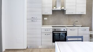 A modern kitchen with a built-in oven, a sink, and a dining area with a table and chairs. - P011 - Porto Recanati, new studio facing the sea (Porto Recanati)