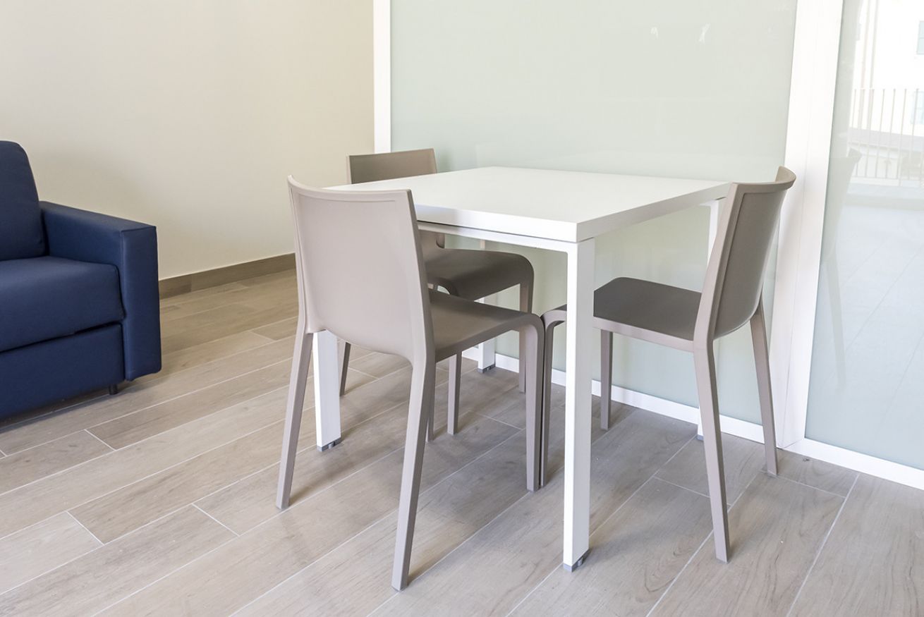 A modern room with a white table and four chairs, a blue sofa, and a glass partition.