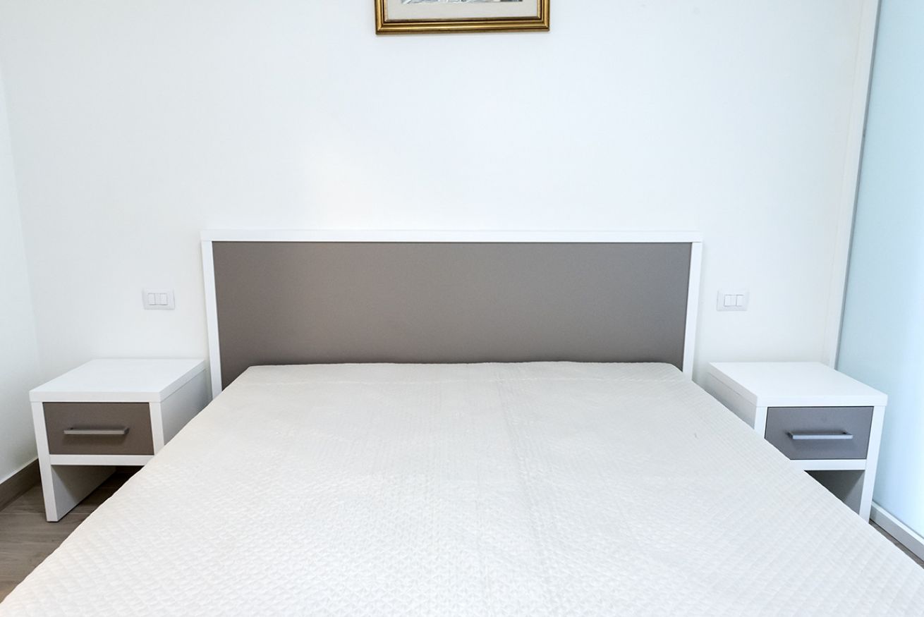 Un dormitori minimalista amb un llit individual, dues taules de nit i un quadre al mur.