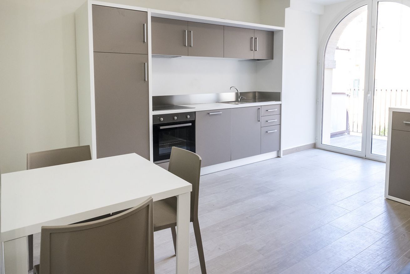 Une cuisine moderne avec des meubles gris, un plan de travail blanc et un coin repas comprenant une table et des chaises.