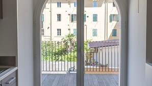 A view through a glass door to an outdoor balcony with a wooden deck, a metal railing, and a building with multiple windows in the background. - A31 - Ancona, new studio apartment in the centre (Ancona)