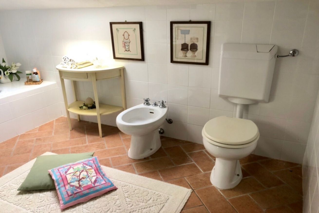 Une salle de bain équipée de toilettes, d’un bidet et d’une petite étagère où sont rangés les articles de toilette.