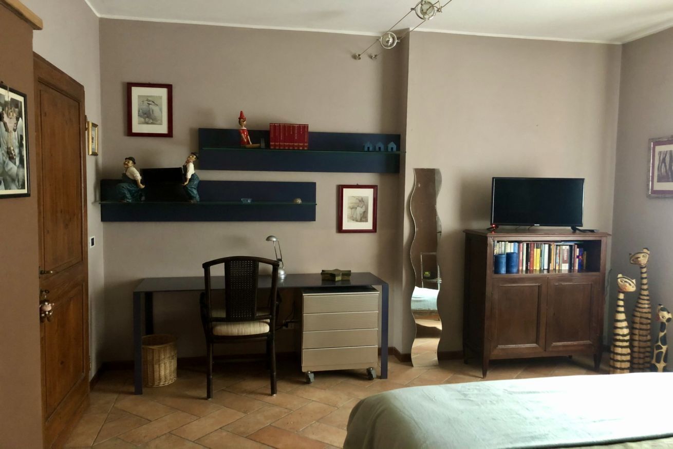 A room with a bed, a desk, a chair, a television, and shelves with books and decorative items.
