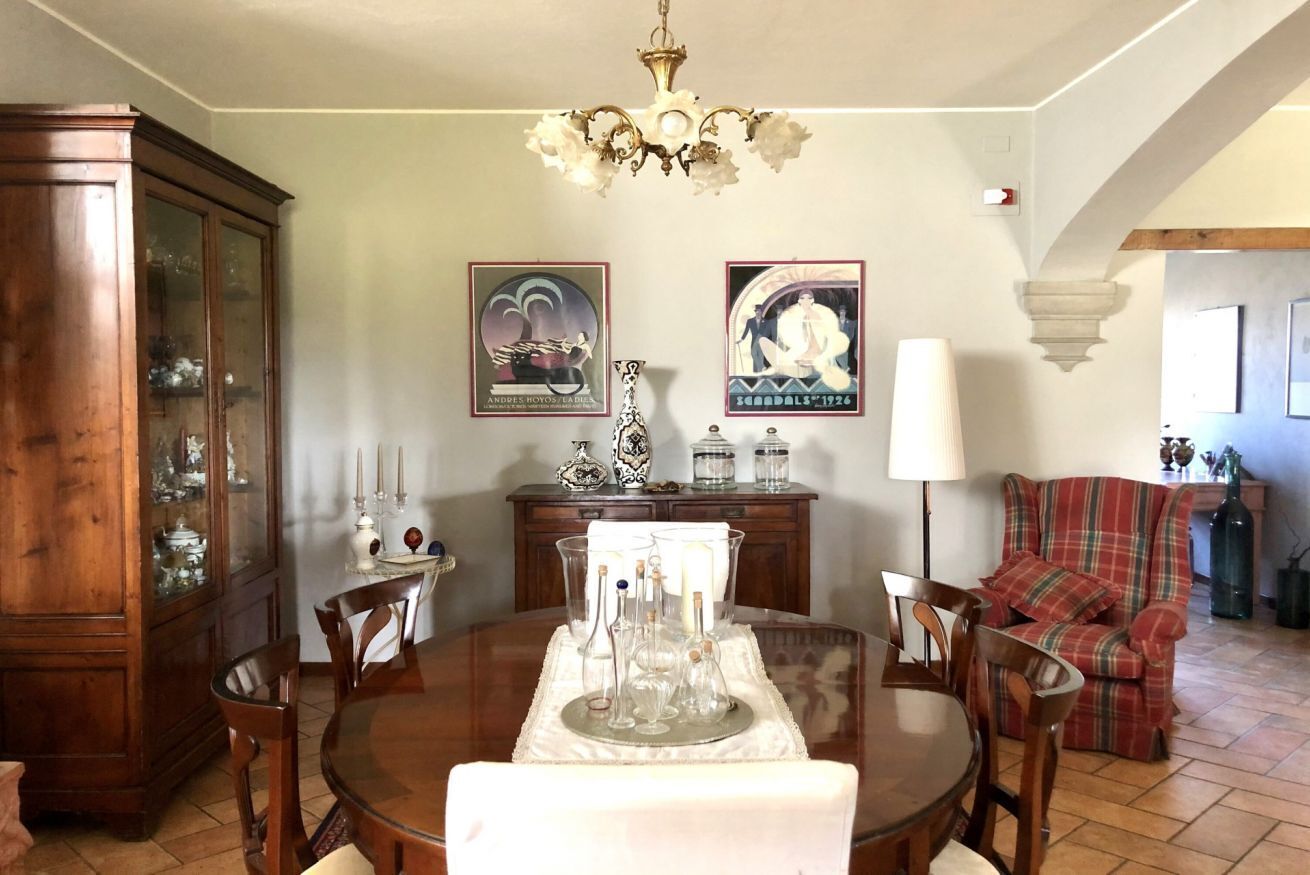 Un comedor con una mesa de madera, sillas, una araña, un armario y un sofá a cuadros.