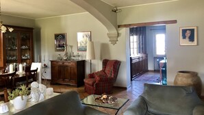 Ein Wohnzimmer mit Esstisch, Stühlen, einem karierten Sessel, einem Glastisch und einem Kamin.