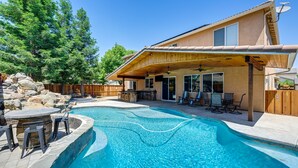 En baghave med swimmingpool, havemøbler og et overdækket udendørs siddeområde.