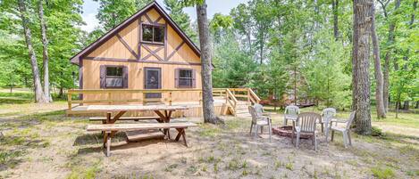 Een houten chalet met een picknicktafel en stoelen, gelegen in een bos.