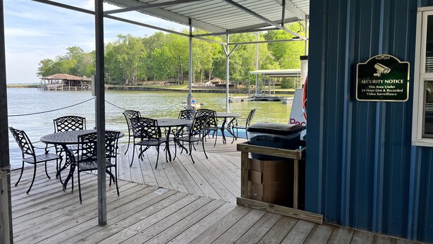 Un espace extérieur abrité, doté de tables et de chaises, avec vue sur un plan d’eau, et un panneau indiquant les consignes de sécurité est affiché sur le mur.