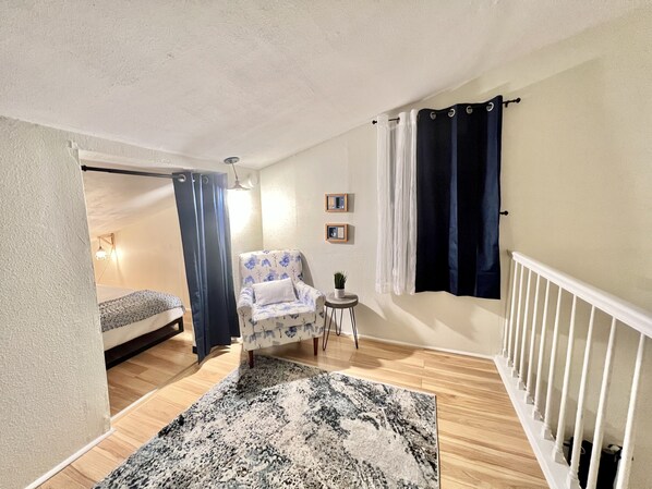 Una habitación pequeña con una cama, una silla, una mesita con una planta y una escalera.