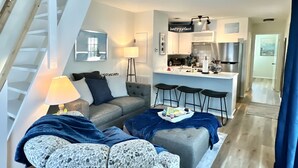 Un appartement moderne doté d’un escalier, d’un espace de vie avec un canapé et un pouf, d’une cuisine avec un coin bar et d’une table à manger.