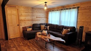 A cozy cabin interior with a wooden floor, a brown leather sofa, a coffee table, and a fireplace. - Haywire Haus, Pictured Rocks, Hot Tub, ORV Trail (Shingleton)