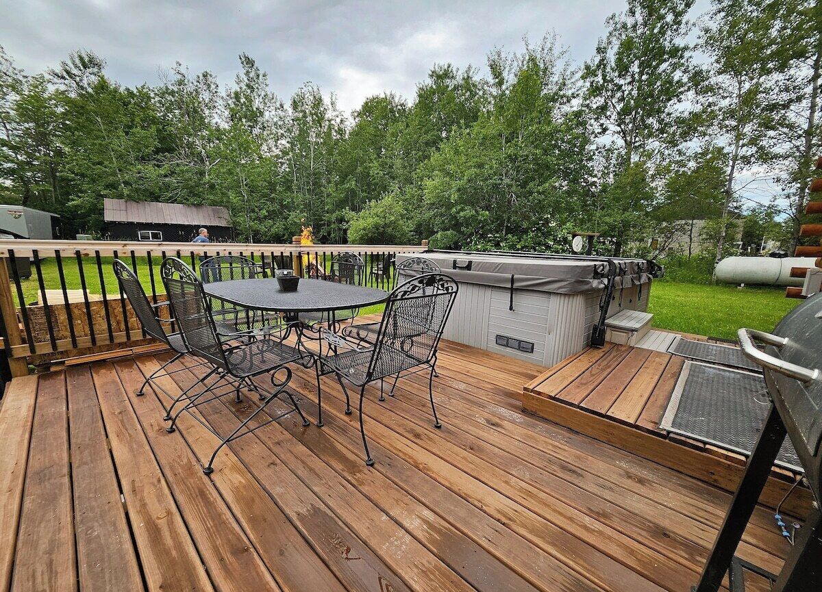 Una terraza de madera con una mesa redonda y sillas, un jacuzzi y una zona de barbacoa.