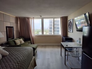 A hotel room with a bed, a desk, a chair, a television, and a window with a city view.
