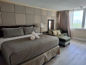 A hotel room with a large bed, a sofa, a TV, and a window with curtains.
