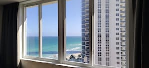 Janela com vista para o oceano e um prédio alto ao fundo.