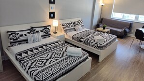A modern hotel room with two beds, a sofa, a small table, and a window.