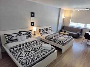 Quarto de hotel moderno com duas camas, um sofá, uma mesa pequena e uma janela.