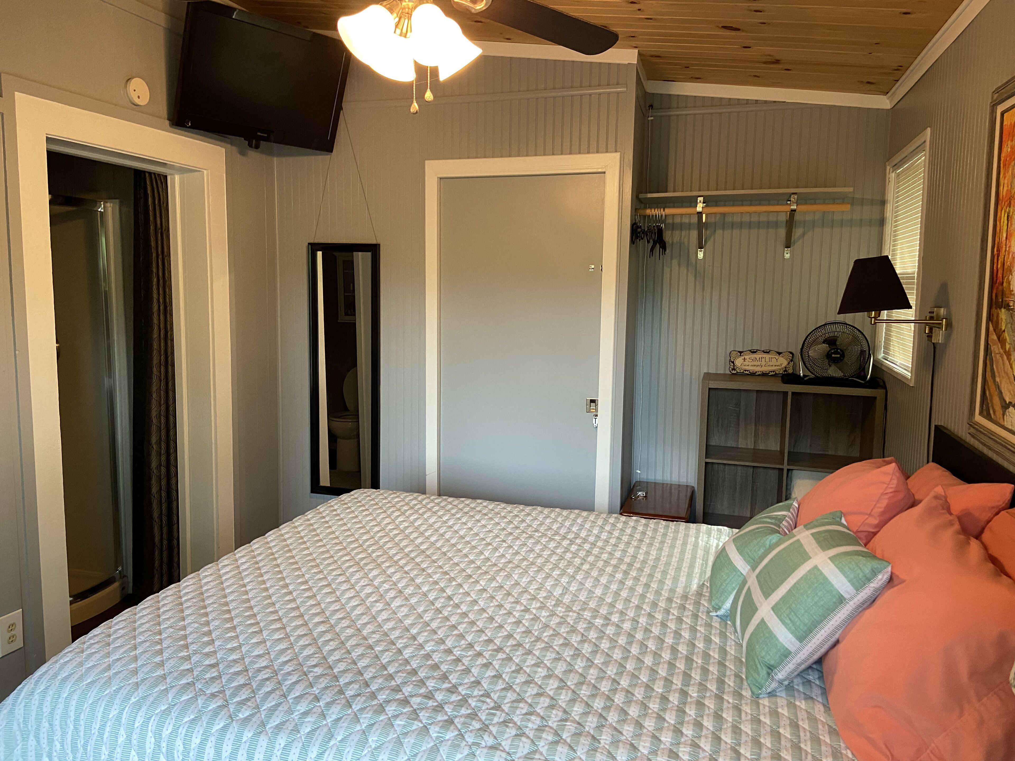 A bedroom with a bed, a ceiling fan, a TV mounted on the wall, and a window with blinds.