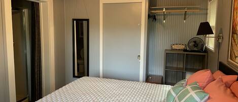 A bedroom with a bed, a ceiling fan, a TV mounted on the wall, and a window with blinds.