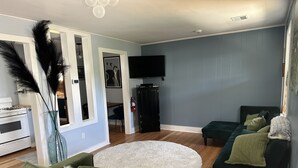 Un salon avec un canapé vert, un tapis blanc et moelleux, un divan vert foncé et un téléviseur à écran plat fixé au mur.