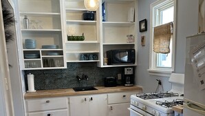 Une cuisine avec des meubles blancs, une cuisinière à gaz, un four à micro-ondes et un évier.
