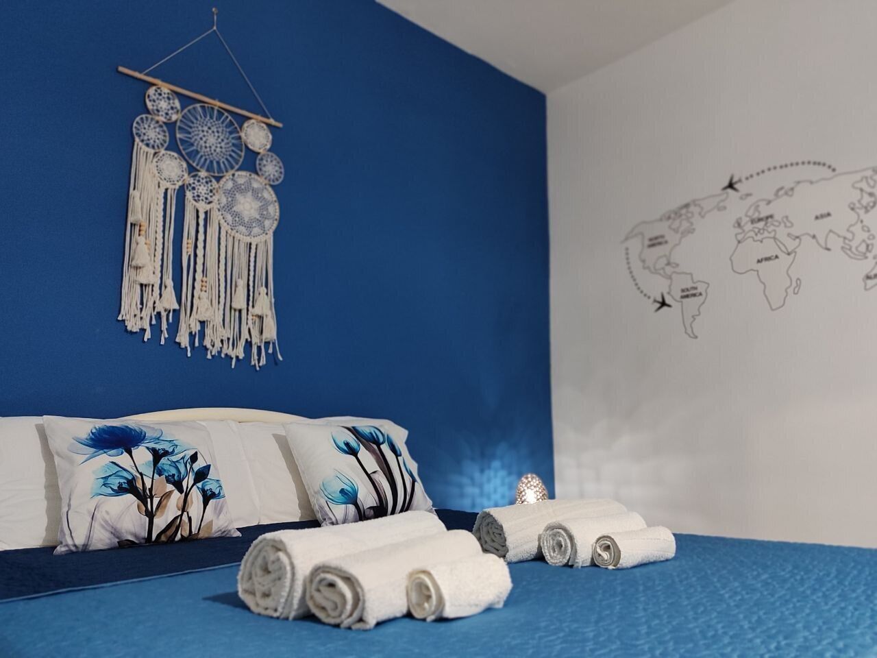 A bedroom with a blue wall, a world map, and a hanging dreamcatcher.