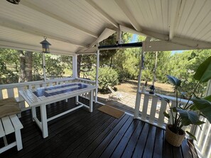 A covered patio with a table and chairs, surrounded by wooden railings and potted plants.