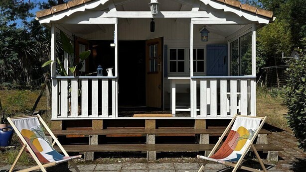 Eine kleine, weiße Holzhütte mit Veranda und zwei Strandstühlen.