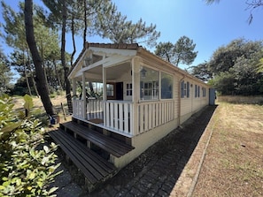 A small, single-story cabin with a porch and a bench, surrounded by trees.