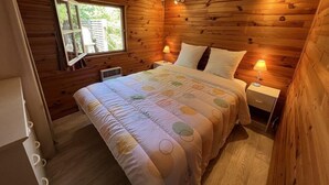 Ein gemütliches Schlafzimmer in einer Holzhütte mit einem großen Bett, zwei Nachttischen mit Lampen, einem Fenster mit Blick auf Grünflächen und einer Decke mit strukturierter Musterung.