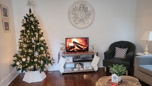 A cozy living room with a Christmas tree, a fireplace, a comfortable armchair, and a round coffee table.