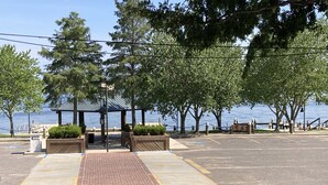 A parking area with a brick pathway leading to a gazebo by the water.