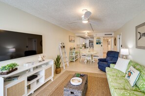 A living room with a flat-screen TV, a ceiling fan, a green patterned sofa, and a dining area in the background.