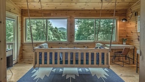 A cabin interior with a wooden deck, large windows, a desk, and a chair.