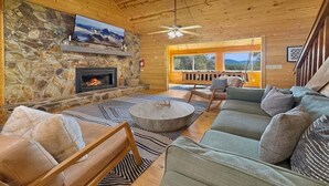 A cozy cabin interior with a stone fireplace, a large sofa, and a television mounted on the wall.